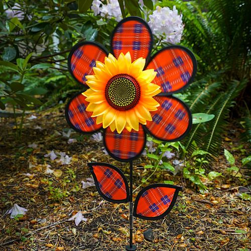 Decorative red and black flower spinner with yellow sunflower center, garden stake with same plaid design leaves in a natural setting.