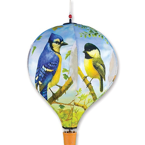 Decorative hanging hot air balloon spinner with blue and yellow birds on a branch against a blue sky.