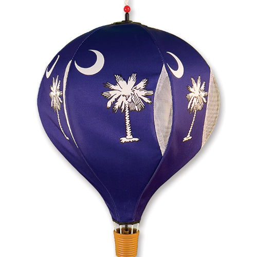 A hanging hot air balloon featuring a deep blue fabric body with embroidered white crescent moons and palm trees, plus a small orange basket base