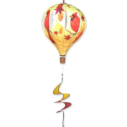 A hot air balloon-shaped wind spinner featuring a printed design of red cardinals, autumn leaves, and a yellow-and-white striped balloon body with a brown basket, plus a long spiral ribbon tail in yellow, red, and brown.
