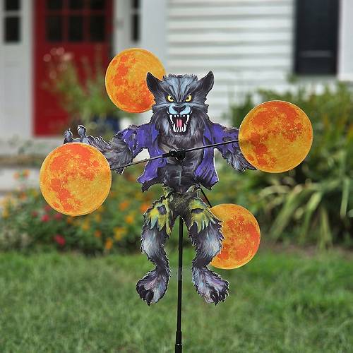 Werewolf Halloween whirligig spinner staked in a yard flower bed with spinning moons