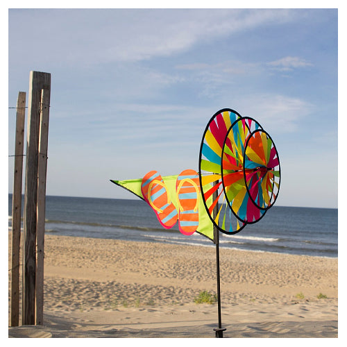 Colorful triple-wheeled wind spinner featuring flip flops on a beach with ocean and sky in the background