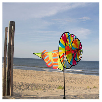 Colorful triple-wheeled wind spinner featuring flip flops on a beach with ocean and sky in the background