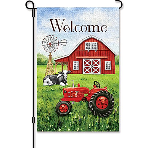 Garden size flag displayed on a black metal garden stake, featuring a watercolor illustration of a red barn, vintage red tractor, black and white Holstein cow, and windmill on a lush green field with the word "Welcome" in dark lettering at the top.