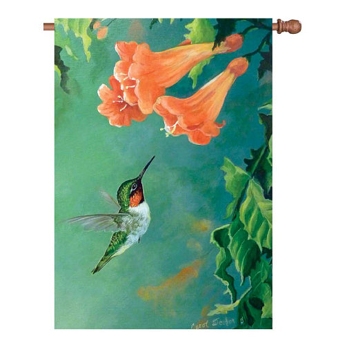 A vertical house flag featuring a painted scene of a hummingbird near orange trumpet flowers against a teal-green background, shown hanging from a wooden flag pole