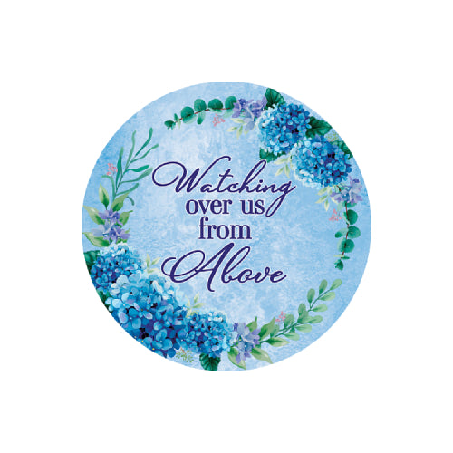 A round decorative sign or sticker with a watercolor-style blue floral wreath and the phrase 'Watching over us from Above' in purple script, shown on a plain white background.