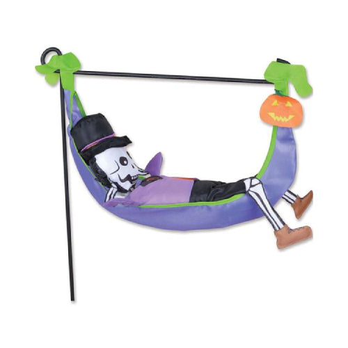 Halloween hanging decoration featuring a skeleton reclining in a purple hammock with green straps and an orange jack-o'-lantern accent, shown on a garden flag stand (not included)