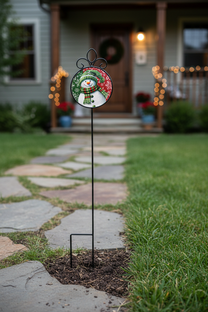A metal garden stake with an interchangeable Suncatcher at the top featuring a snowman wearing a green hat and scarf against a red and green patterned background.